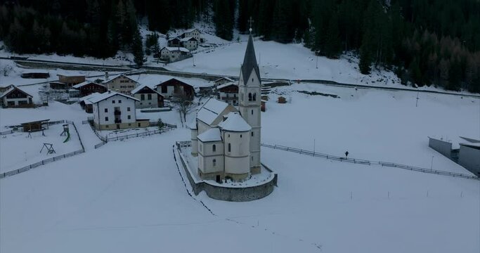 Orbiting aerial view of snow-covered church building in the quaint village of Trafoi beside the Stelvio Pass road.