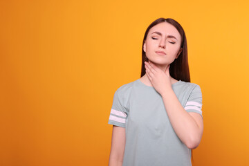 Obraz premium Young woman with sore throat on orange background. Space for text