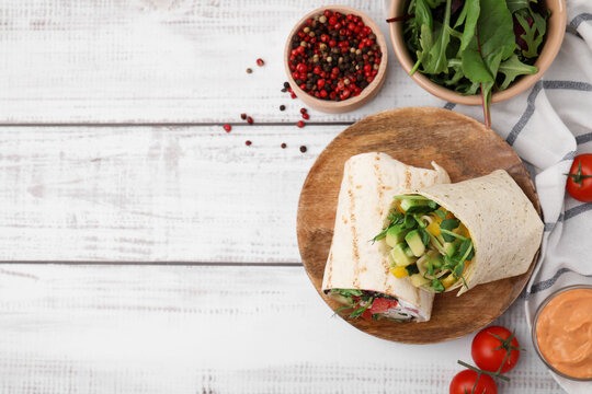 Delicious sandwich wraps with fresh vegetables, tomatoes, sauce and peppercorns on white wooden table, flat lay. Space for text