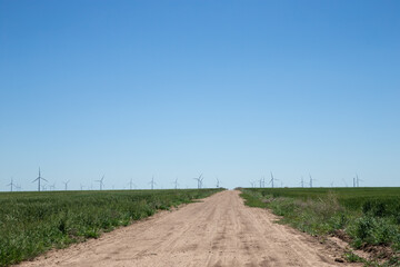 Grouping of windmills at windmill farm on hot day with heat rising from the wheat fields down a lonely country dirt road