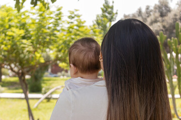 Madre y bebé en el parque, de espaldas, cabello lacio, día de verano