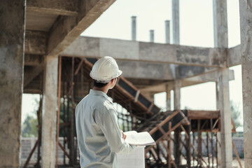 Behind Architect wearing safety helmet working with blueprint for inspection building in construction site.