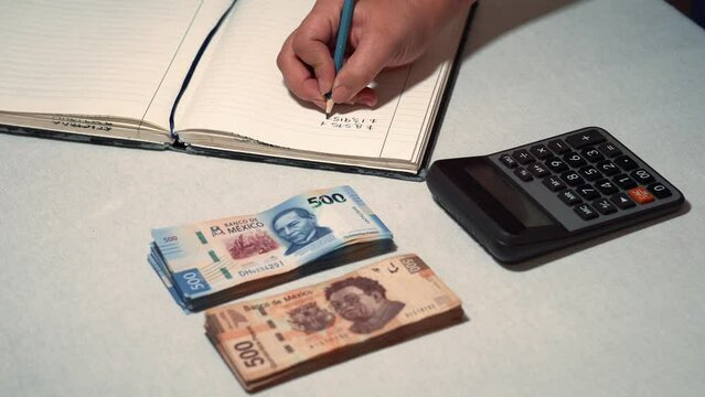 Persona haciendo cuentas finanzas economicas con billetes mexicanos en calculadora con cuaderno papel y lapiz sobre un escritorio