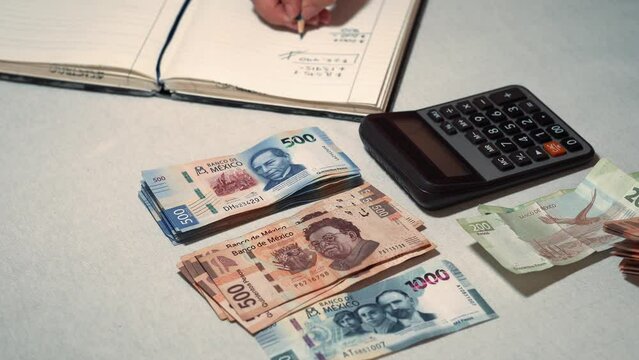 Manos de una persona sola sin rostro esta haciendo cuentas fiscales econ&oacute;micos con billetes mexicanos y calculadora