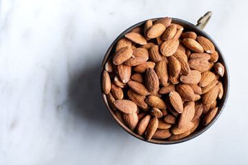 Bowl of fresh almonds in a bowl on white marble background. Top view.