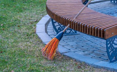 A broom for cleaning near a park bench.