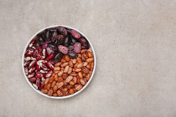 Bowl with different types of beans on light grey table, top view. Space for text