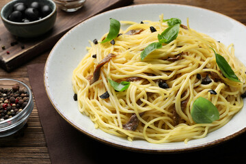 Delicious pasta with anchovies, olives and basil on wooden table, closeup