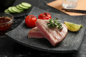 Pieces of delicious tuna with microgreens, lime and tomatoes on table, closeup