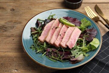 Pieces of delicious tuna steak with salad served on wooden table, closeup