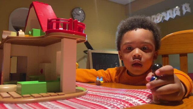 Three-year-old cute black child playing with his toy house at home