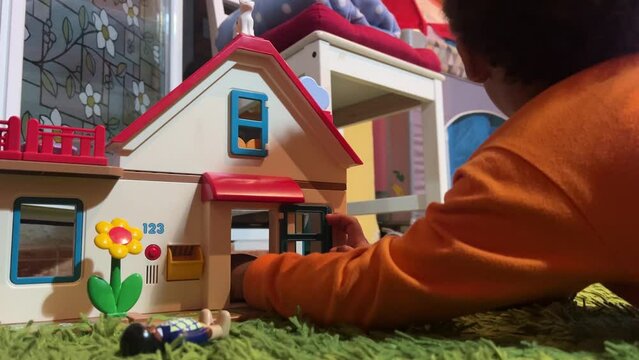 3-year-old black child playing with his toy house at home, lying on a green rug, wearing an orange long sleeve shirtj.