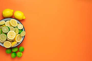An enamel bowl with fresh halved and sliced lemons and limes and whole citrus fruits on an orange background.