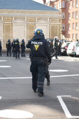 Security, authority and back of police officer in the city working to patrol a protest or march. Law enforcement, public service and safety guard in uniform for protection in an urban town street.