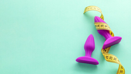 Sex toy size. Purple anal plugs and yellow measuring tape on a green background. Copy space for text