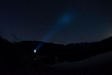 Adventurous man looking at the stars on a rocky beach in the Pacific Northwest at night with his headlamp shinning up at the stars.  © Pelo Blanco Photo