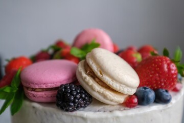 Birthday or anniversary cake with cream cheese frosting decorated with macaroons, fresh raspberries, strawberries, blackberries and blueberries. 