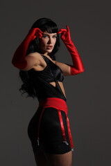 Pinup vintage girl lay on floor in lingerie.  Black wig, underwear, stockings and red gloves, big lips and eyes. Beautiful posch woman portrait, grey background