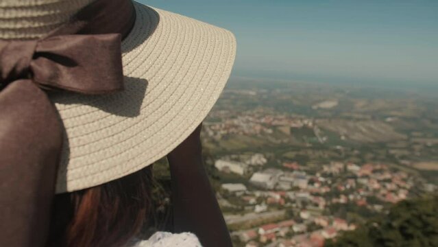 Rear view of attractive female torist in a straw hat, taking pictures of stunning views of San Marino with camera