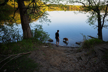 Man and Dog with Feet in Lake Water Off Park Path