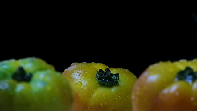 Water splashing over three big yellow beefsteak tomatoes with black background (static close-up shot)
