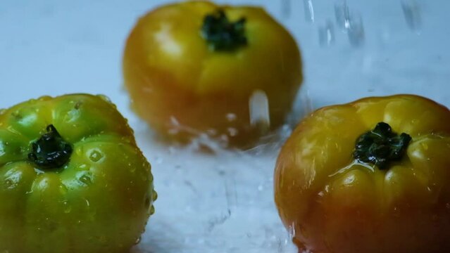 waterdrops splash coming down onto three big beefsteak tomatoes on a white surface (close-up shot)