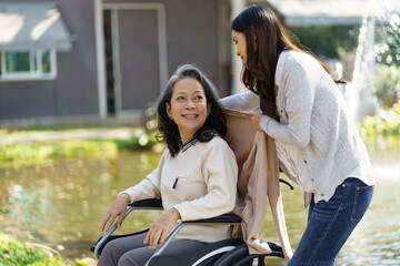 Asian senior woman in wheelchair with happy daughter. Family relationship retired woman sitting on wheelchair in the park age care at retirement home.