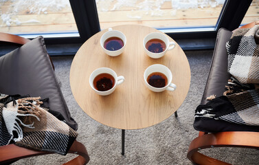 Four cups of fresh brewed tea on small table and cozy designed chairs with checkered plaids in cafe. Above view of white mugs on wooden table with chairs on sides in frosty morning. Concept of rest.