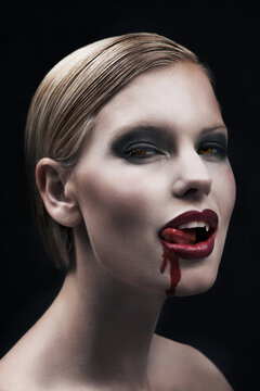 Portrait, blood and a woman vampire in studio on a dark background for halloween or cosplay. Fantasy, horror or scary with an attractive young female monster posing as an evil and feminine creature