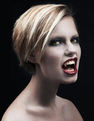 Portrait, fangs and a woman vampire in studio on a dark background for halloween or cosplay. Fantasy, horror and scary with an attractive young monster posing as an evil or supernatural creature