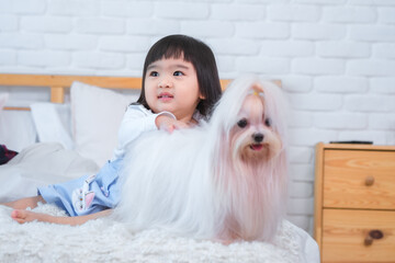 Little girl looking a sideway and white dog on bed in bedroom.