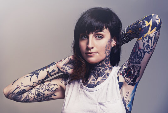 Portrait, tattoo and edgy with a woman in a tank top on a studio gray background for contemporary style. Fashion, body art and punk with an attractive young female model posing to show her ink