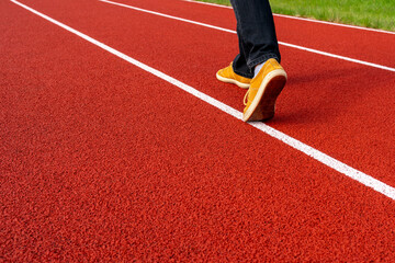 Man in brown sneakers and black jeans walk alongside a white line on a red running track