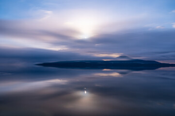 Fototapeta na wymiar 雲の向こうに太陽の輝く空を水面に反射する朝の湖。北海道の屈斜路湖。