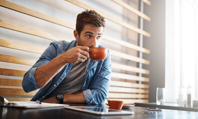 The perks of being the owner, free coffee. a handsome young man drinking coffee while working in a coffee shop.