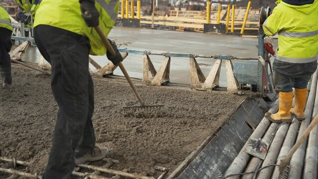 Construction workers raking fresh asphalt at industrial building site.