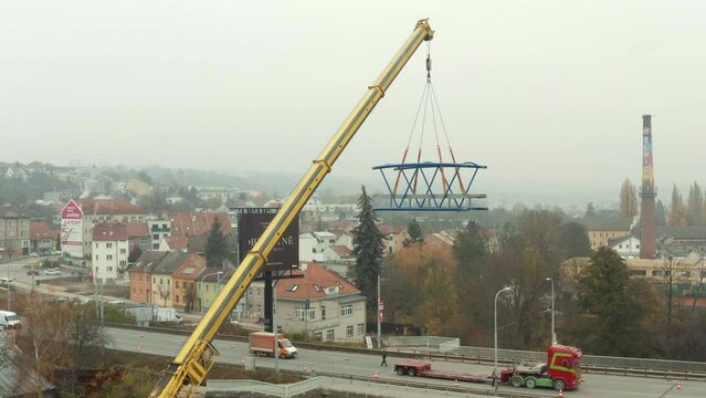 Mobile crane slowly moving new bridge segment to load on truck on road.