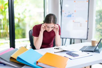 Very stressed business woman and female employee sitting in front of her computer with her hands in front of her eyes, feeling sad and depressed. Too much work - huge pile of paperwork at office table