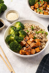 One quinoa bowl with steamed broccoli and smoked tofu cubes in teriyaki sauce with sesame seeds as topping, black chopsticks, grey concrete background