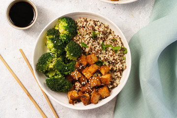 One quinoa bowl with steamed broccoli and smoked tofu cubes in teriyaki sauce with sesame seeds as...