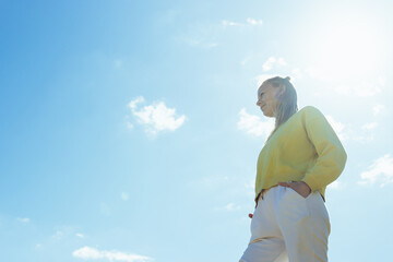 portrait of a girl against the blue sky, the girl is standing in a yellow sweater and white pants, there is a place for an inscription, a beautiful landscape with a girl