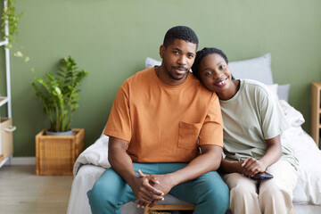 Portrait of affectionate African American couple smiling at camera while sitting on bed at home