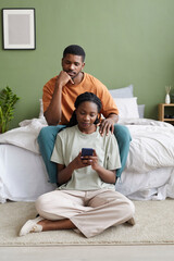 African American young couple using smartphone during leisure time in bedroom at home