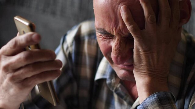 the concept of internet and telephone fraud against pensioners. frustrated grandfather holding his head and smartphone, experiencing the loss of finances from scammers