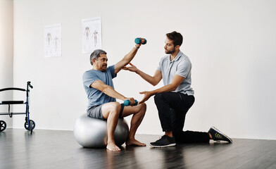 Obraz premium Slow and easy movements. Full length shot of a young male physiotherapist helping a mature male patient with movement exercises at a clinic.