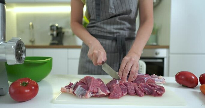 Close-up view of woman cutting up fresh meat with a knife on a kitchen board.