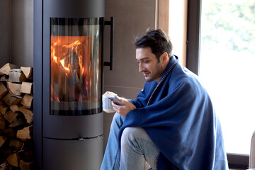 Young man sitting close to the fireplace and warming in cold winter day	
