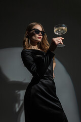 Gorgeous fashionable young chic woman with cool sunglasses in a stylish black elegant dress with a...