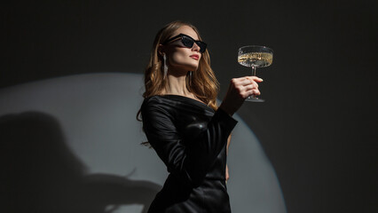 Beautiful elegant young fashion woman with sunglasses in a trendy black dress with a vintage glass...