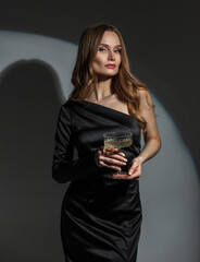 Elegant beautiful young girl in a fashionable black dress with a glass of champagne at a party. Pretty chic Lady celebrates an event - obrazy, fototapety, plakaty